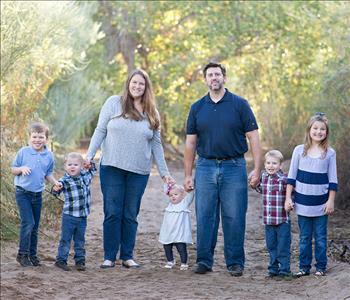 A smiling happy photos with 2 girls, 3 boys and mother and father in the middle holding hands with the kids.